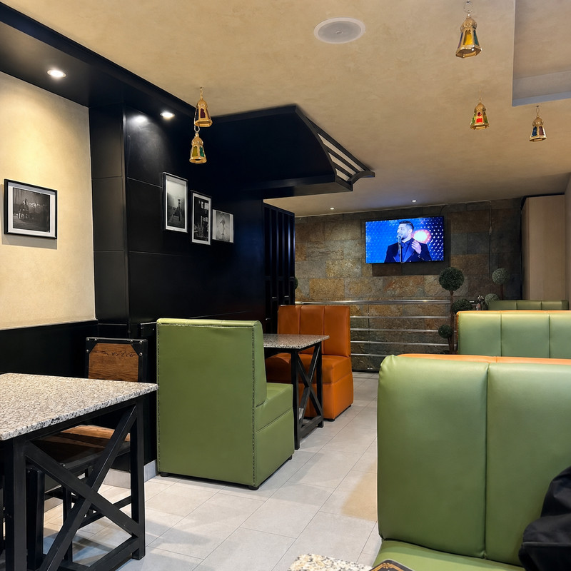 Salle de Melkash alsham avec banquettes vertes et orange et écran au mur