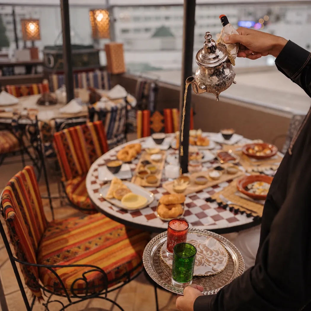 Serveur versant le thé à la menthe au-dessus d'une table de pâtisseries sur la terrasse de Dar El Kaid