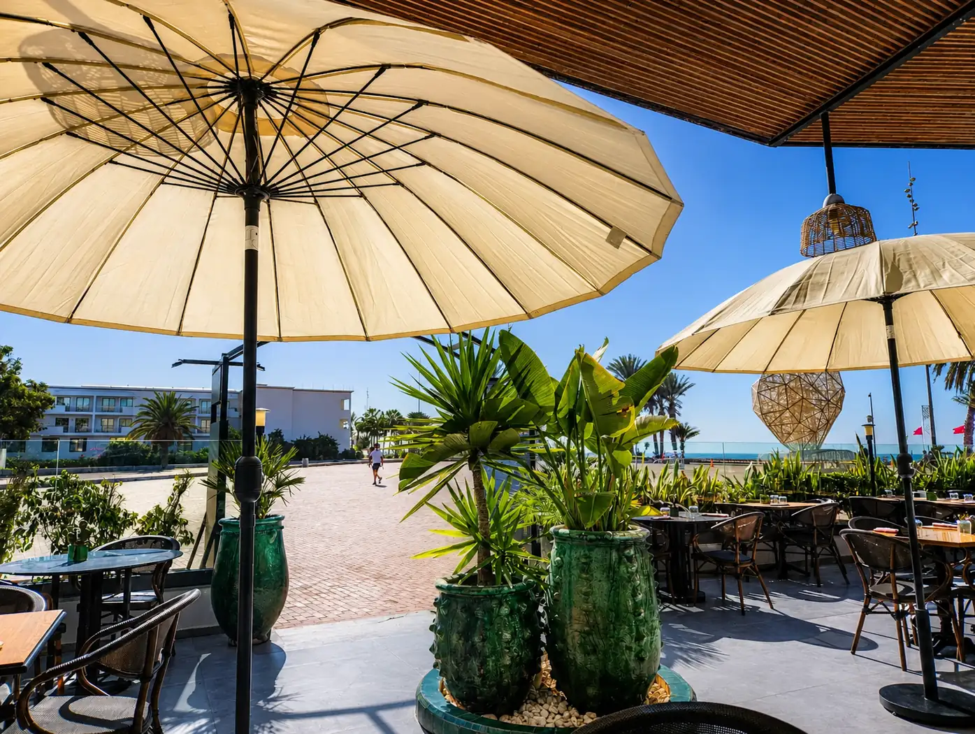 Terrasse du Restaurant Jade à Agadir sous des parasols, avec la promenade et la mer au fond
