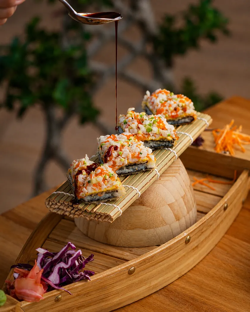Bouchées de sushi garnies sur un bateau en bois, nappées de sauce, chez Bonsaï Marrakech