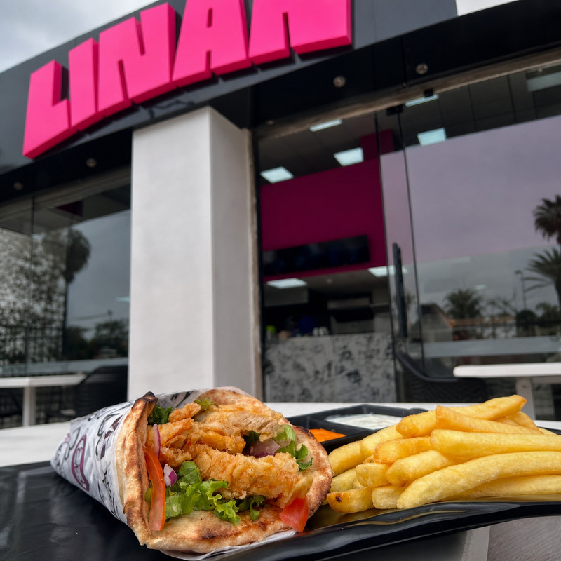 Enseigne rose Linan au-dessus de l'entrée vitrée, wrap et frites au premier plan